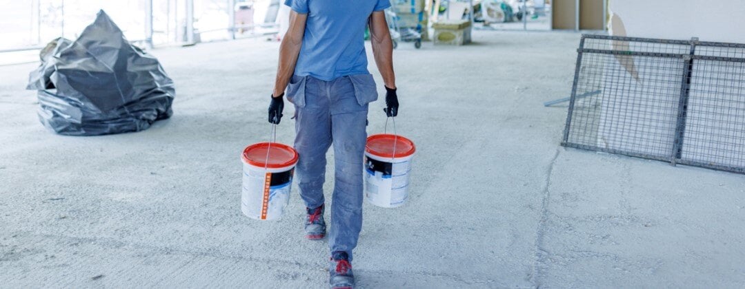 types of adhesives used in construction -- worker wearing hardhat carrying buckets of product through building